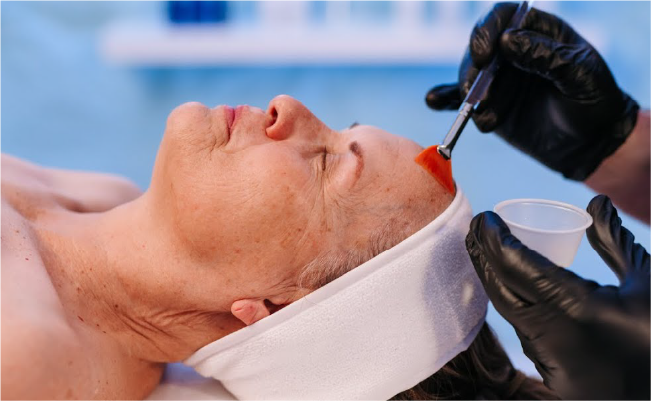 Ältere Frau erhält eine kosmetische Behandlung im Gesicht, die von einem medizinischen Fachpersonal mit schwarzer Handschuhen ausgeführt wird.