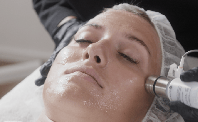 Frau erhält eine Hautbehandlung mit einem Gerät im Gesicht, in einem Behandlungsraum.