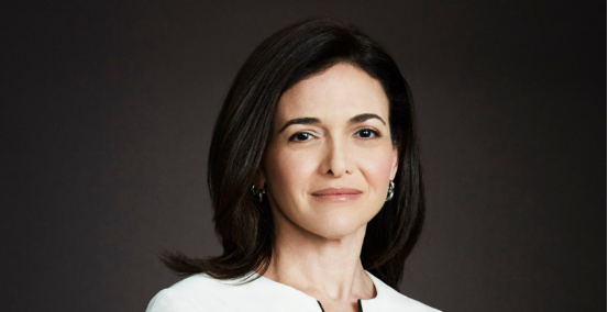 A woman with shoulder-length dark hair wearing a white top against a dark background.