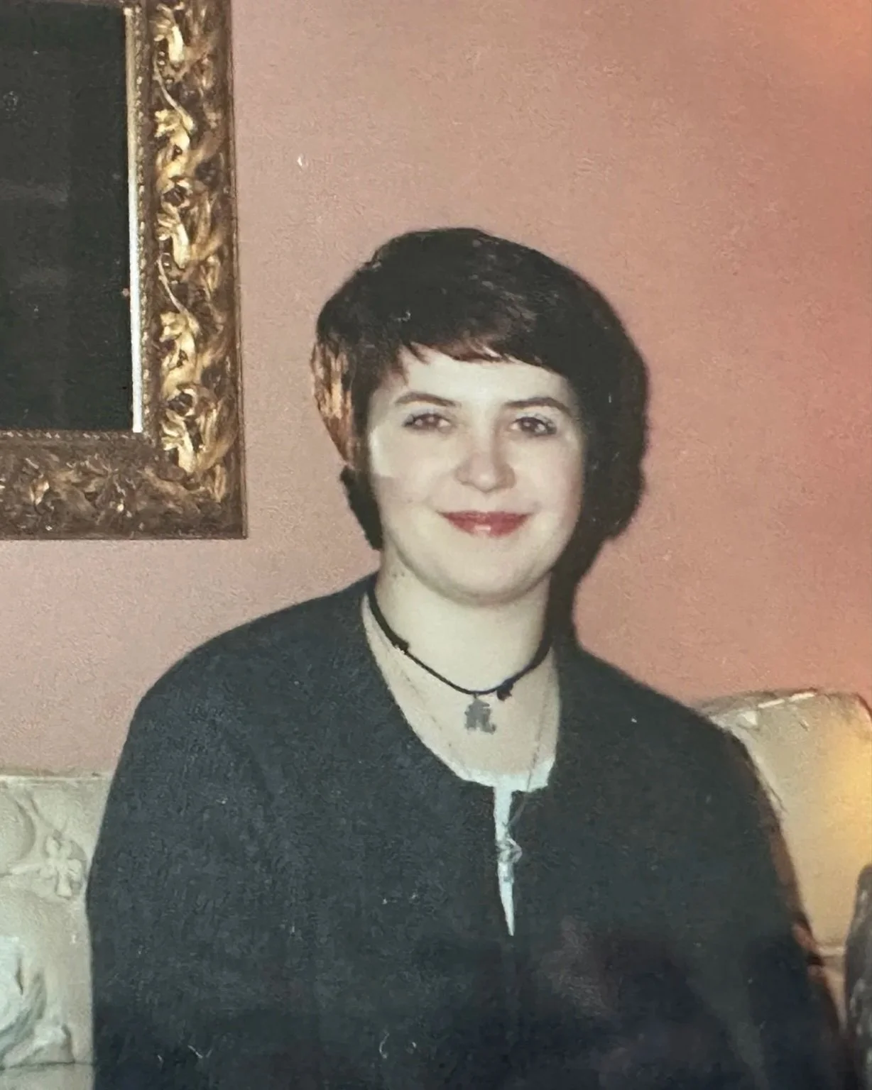 Jackie with short hair sitting on a sofa smiling at the camera in a grey cardigan her Baci bought her.