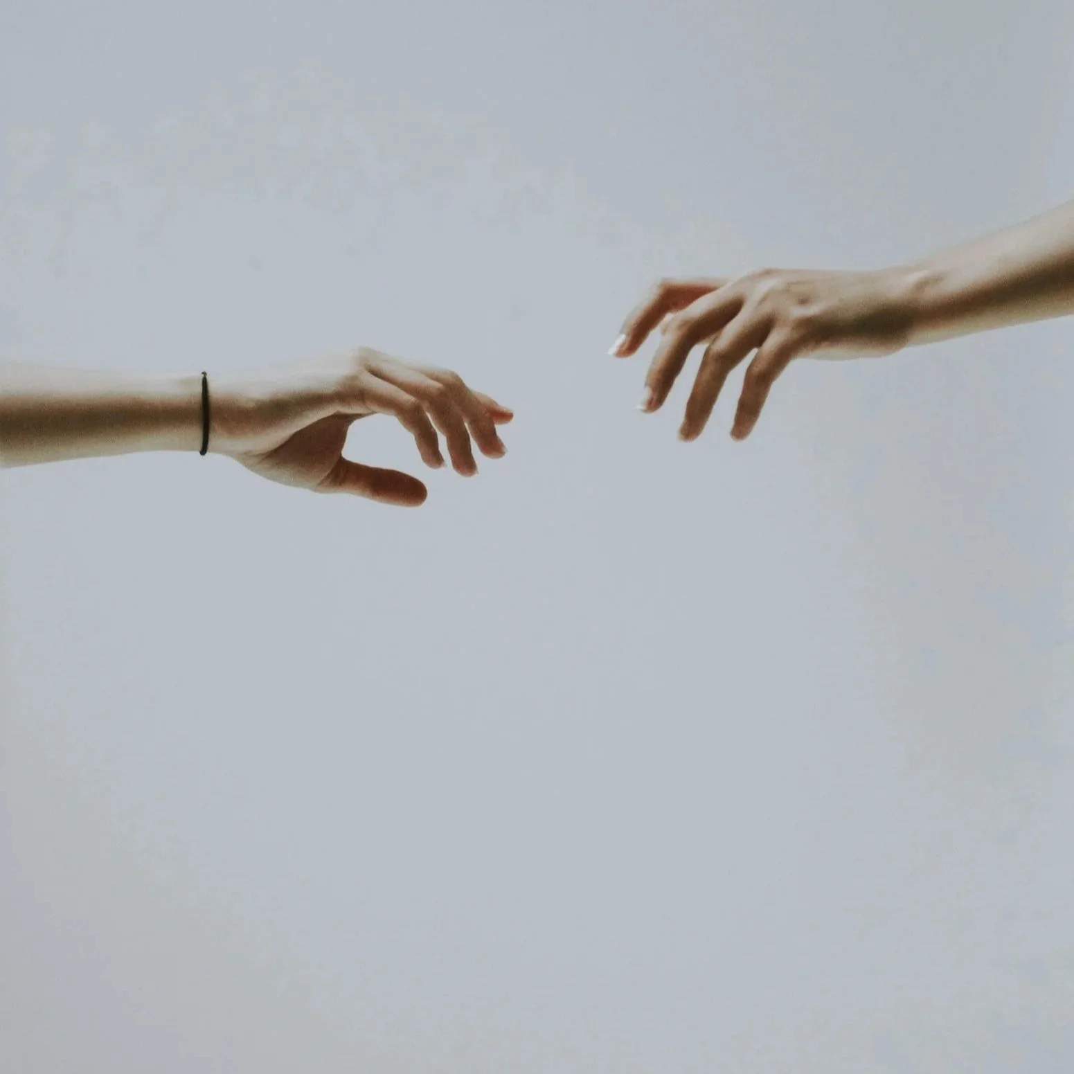 Hands almost touching, blueish white background.