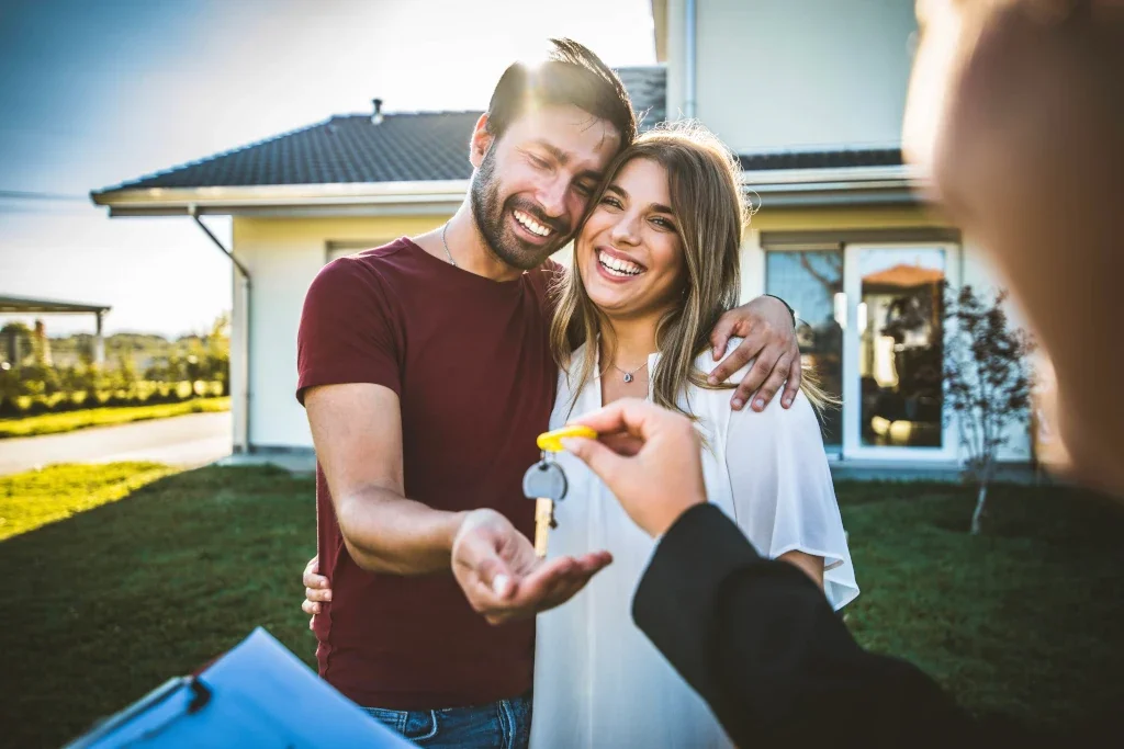 Couple happily accepting house keys from a real estate agent in front of a house.