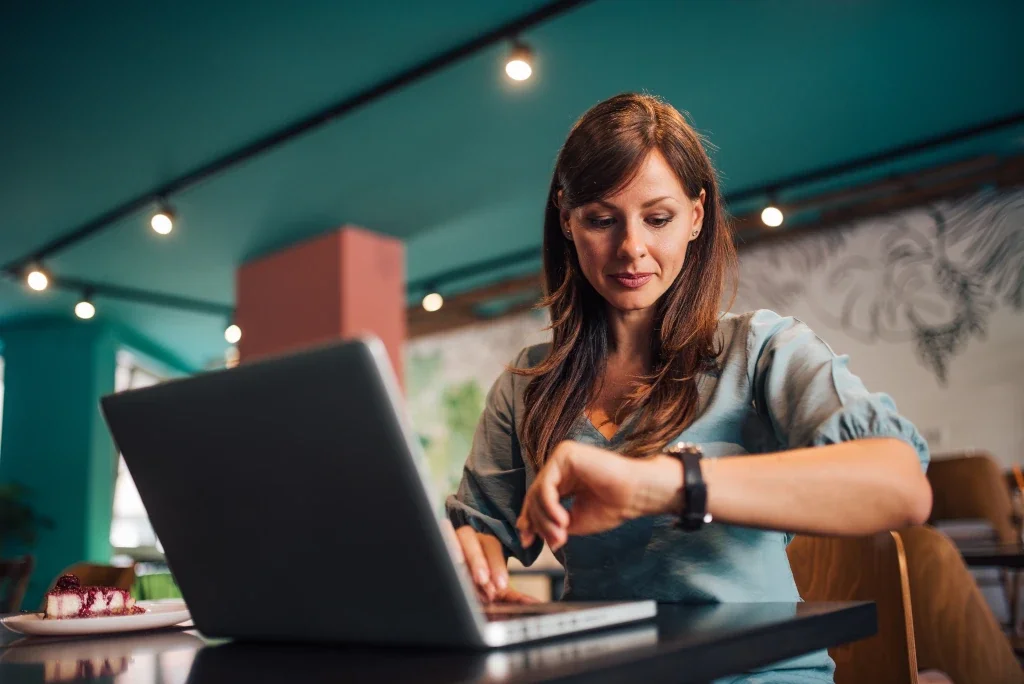 Woman with brown hair checking her smartwatch while sitting at a table in a colorful cafe.