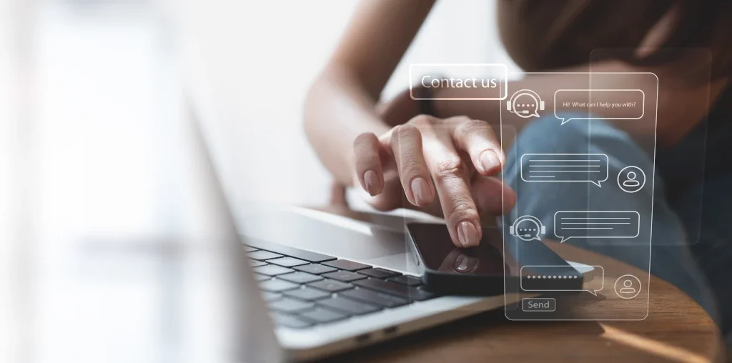 Person using a laptop and mobile phone with a digital overlay of a chat interface that says 'Contact us' and includes chat bubbles, a 'Send' button, and user icons.