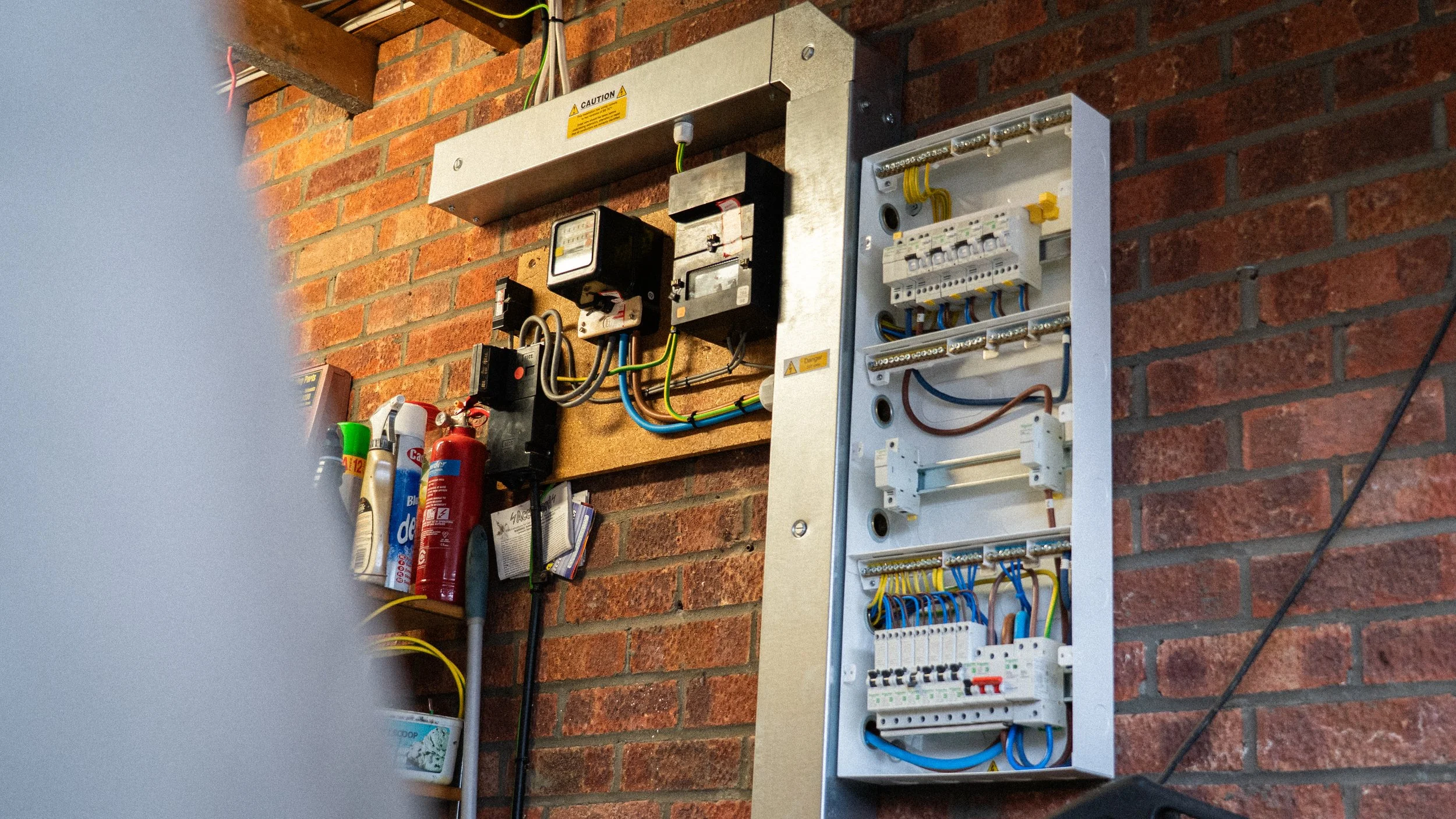 Domestic single phase consumer unit with metal trunking including wiring and components mounted on a brick wall in a garage.