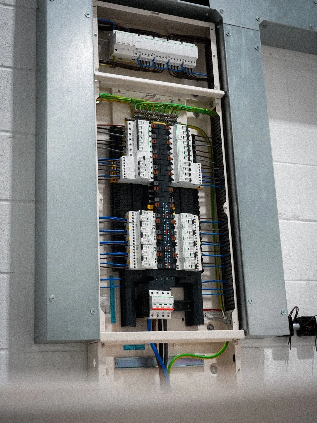 Commercial 3 phase electrical distribution board with circuit breakers, contactors and neat wiring inside a metal enclosure mounted on a white brick wall.