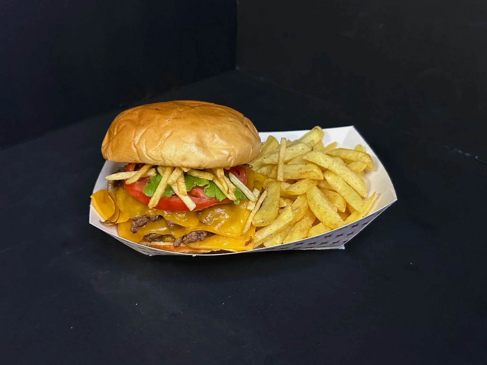 A cheeseburger with lettuce, tomato, cheese, and pickles in a bun, served with a side of French fries on a paper tray.