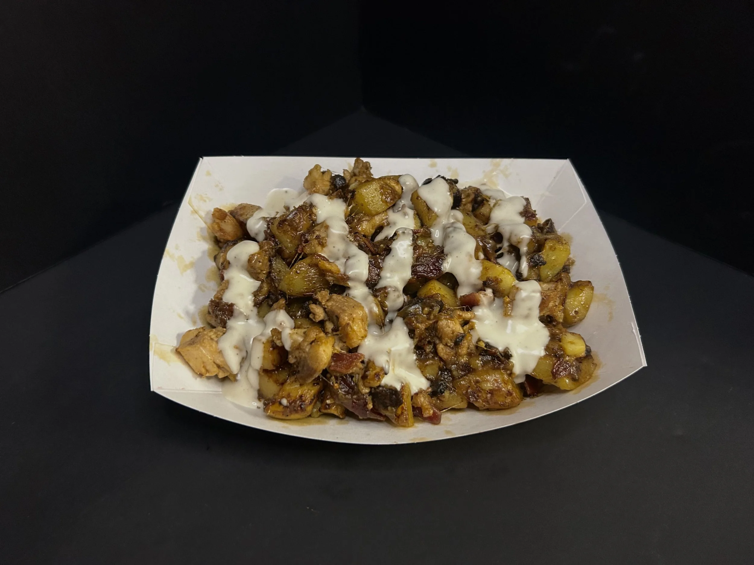 A paper food tray filled with loaded nachos, topped with cheese sauce, sour cream, and various toppings.