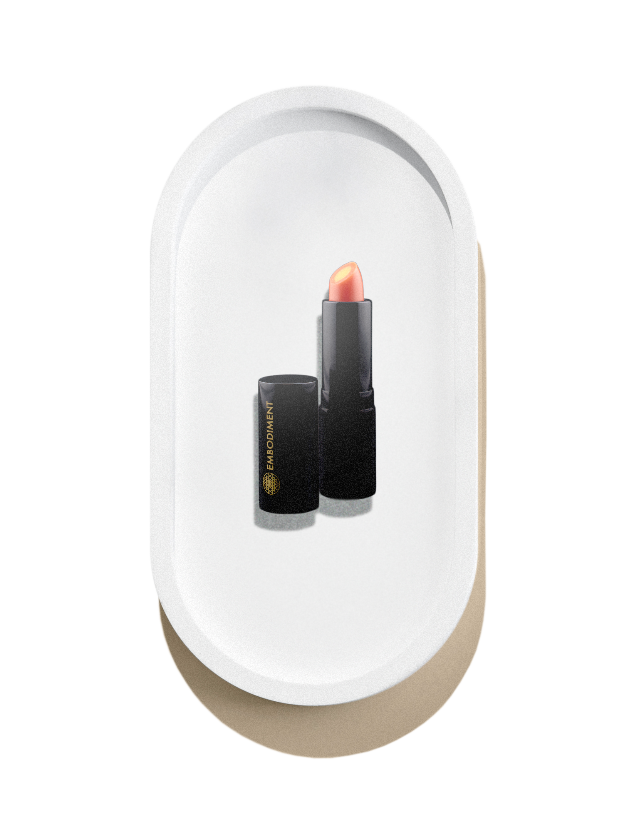 A tube of Embodiment lipstick with the cap removed, revealing the lipstick inside, displayed on a white and beige oval tray.
