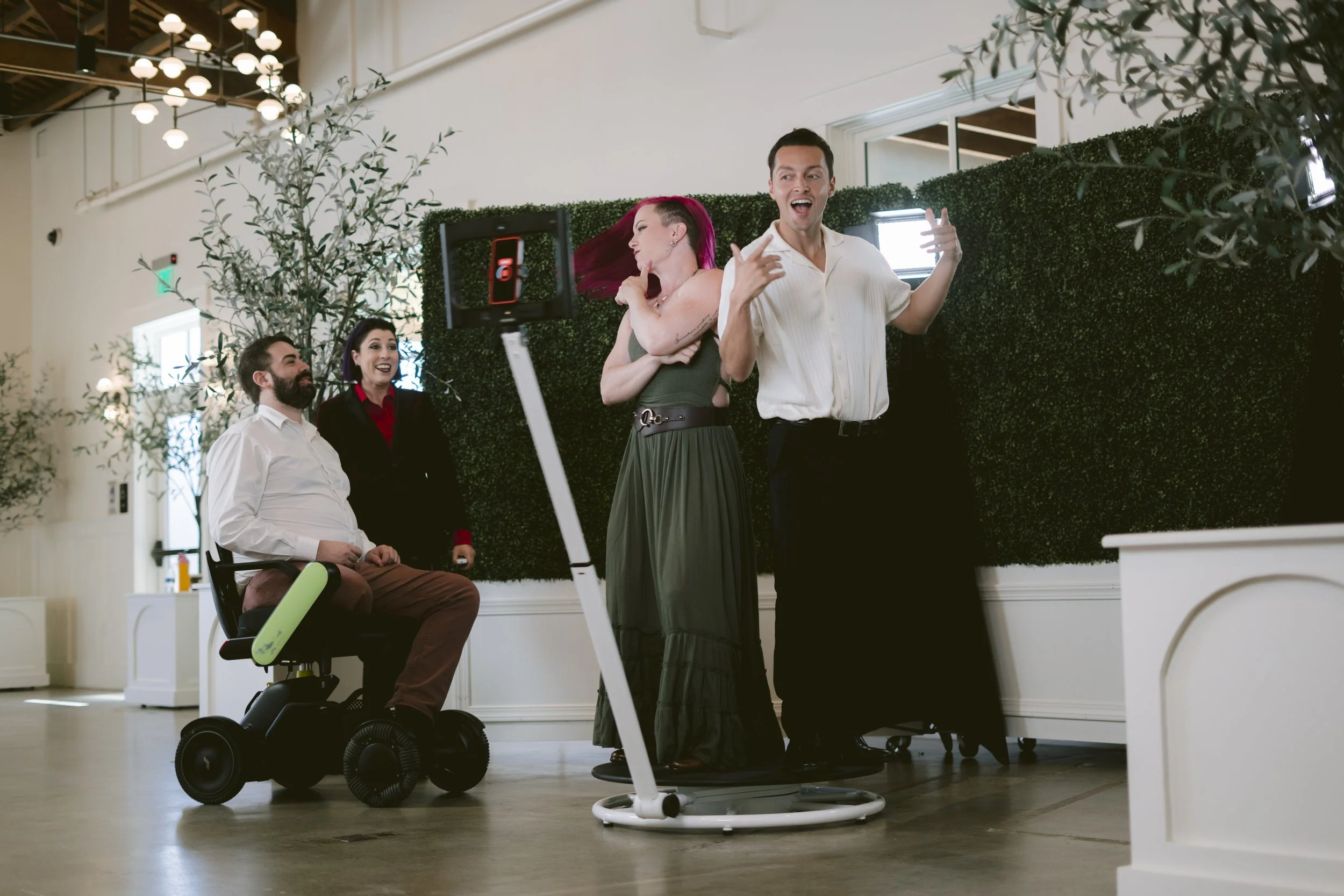 Group of five people enjoying a dance party indoors, with three standing and one sitting in a motorized wheelchair, all smiling and having fun.