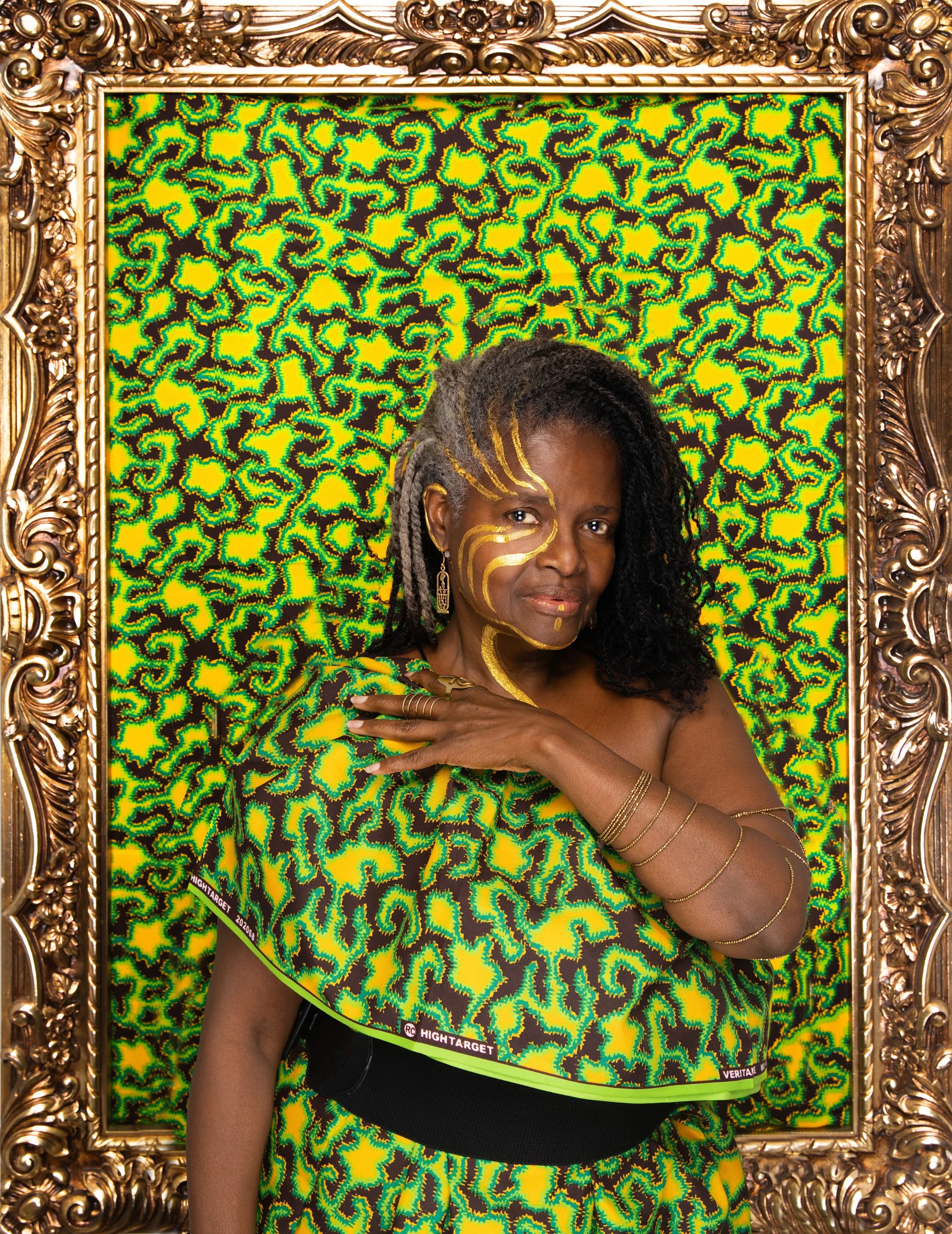 Black woman with gold-painted dreadlocks, vibrant green-yellow patterned dress, and multiple gold bangles, posing in ornate gold frame. Born Rich: Black as My Soul photography series.