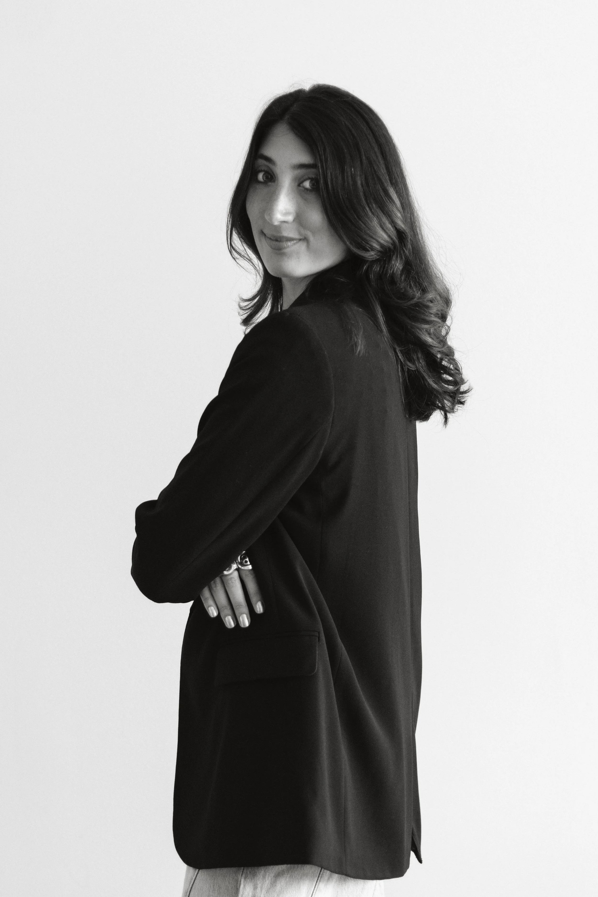 Black and white photo of a woman with dark hair, dressed in a blazer, posing with arms crossed against a plain light background.