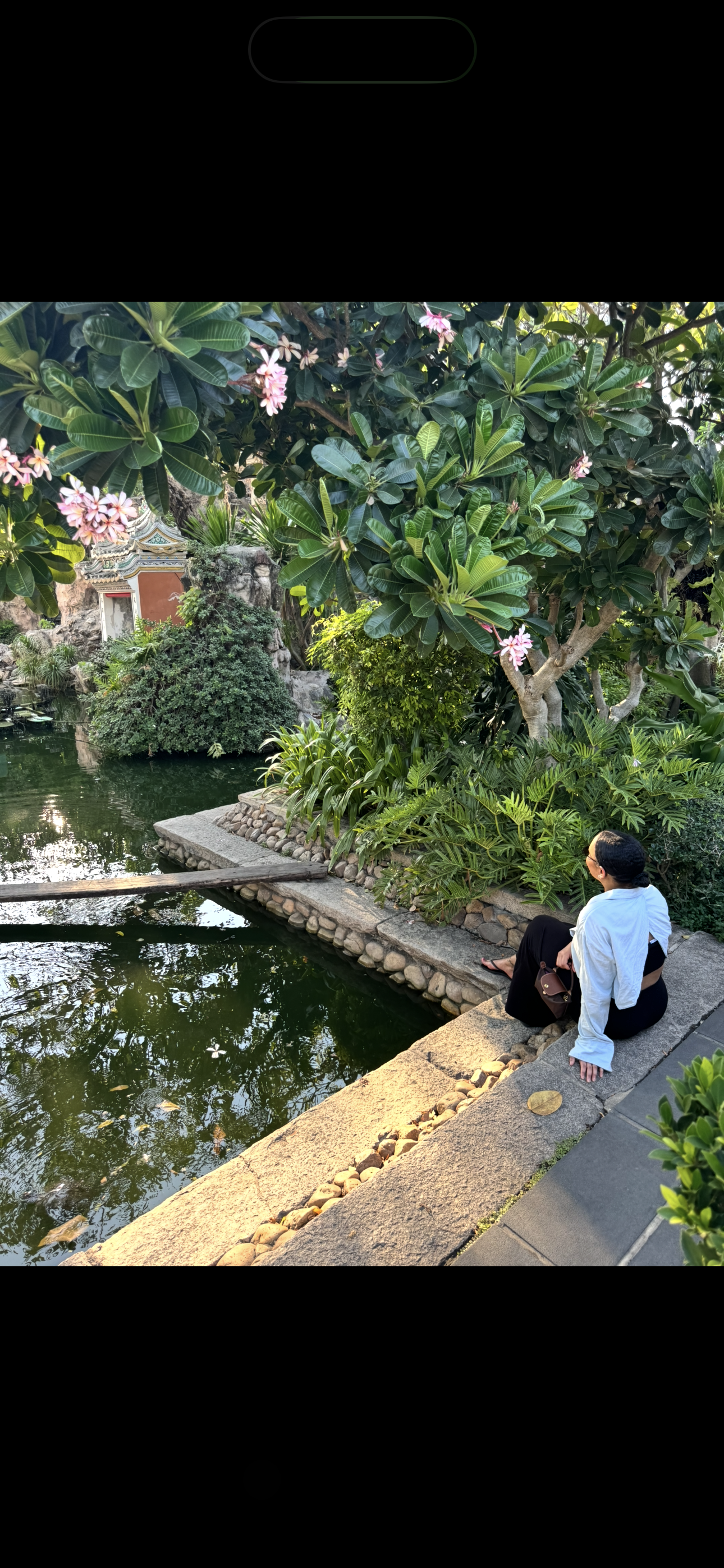 Daniela, founder of PalmSide Atelier sitting beside a pond in lush tropical garden.