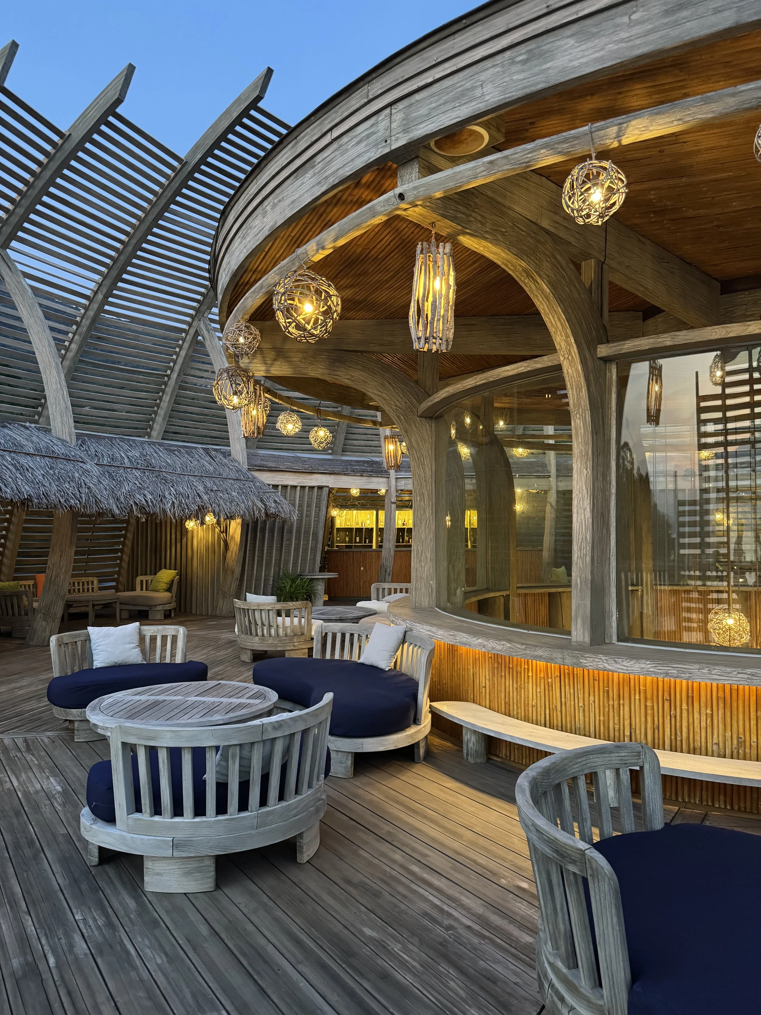 Outdoor Loung at A Lam Retreats Ninh Van Bay , with wooden furniture, navy hanging lights beneath a thatched roof.