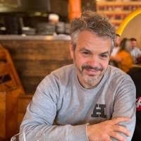 A middle-aged man with gray hair and a beard, smiling at a restaurant or café