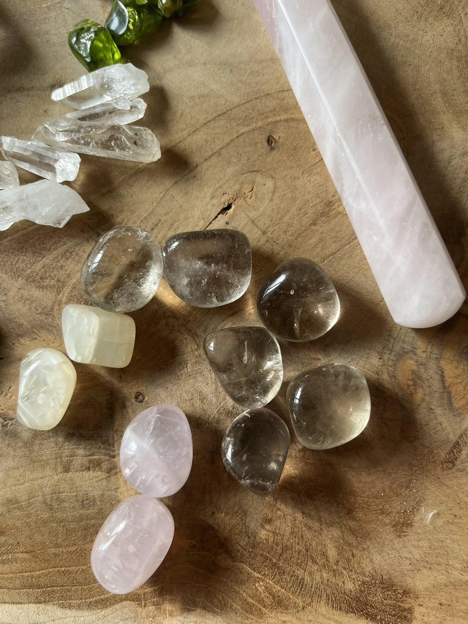 Various polished and raw crystals and stones including clear quartz, rose quartz, and green stones on a wooden surface.