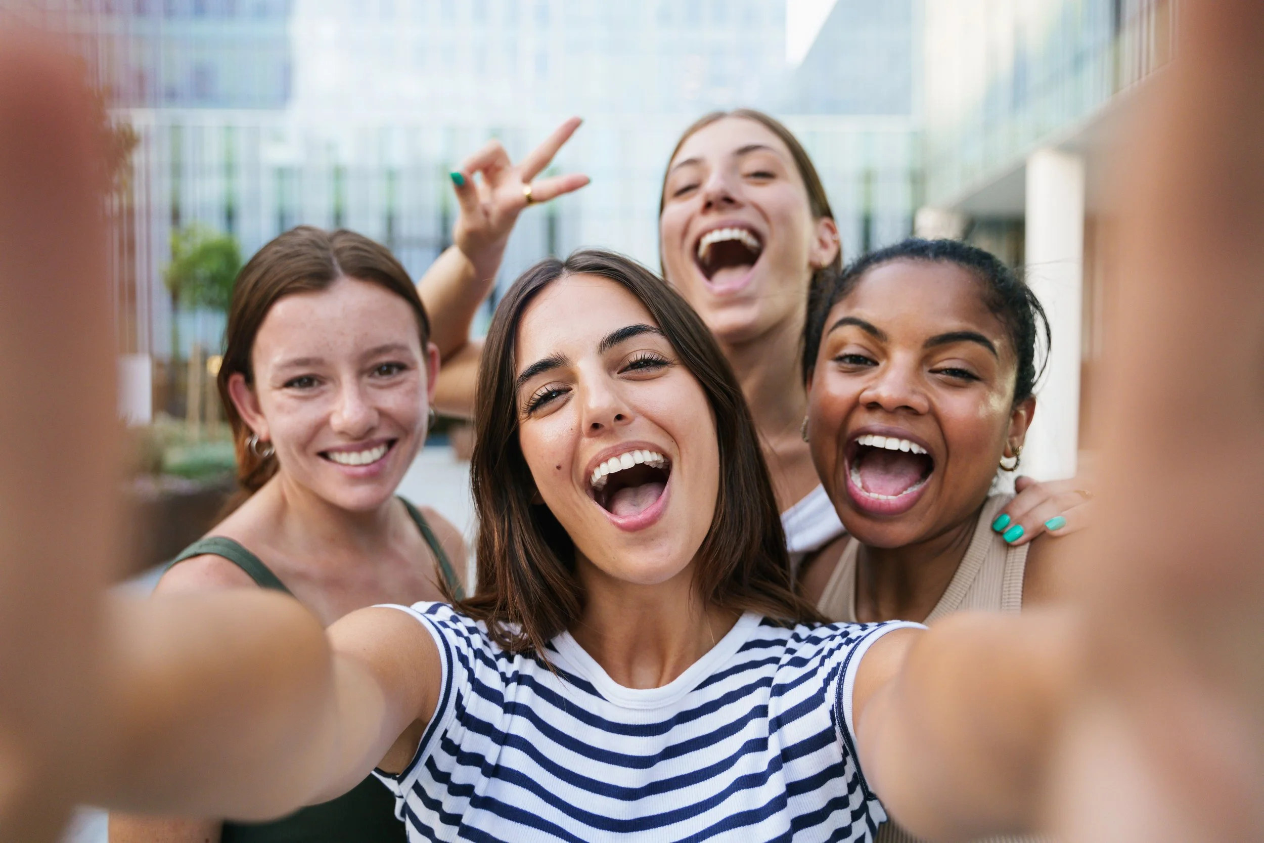 A group of five young women taking a selfie outdoors, smiling, laughing, and enjoying each other's company.