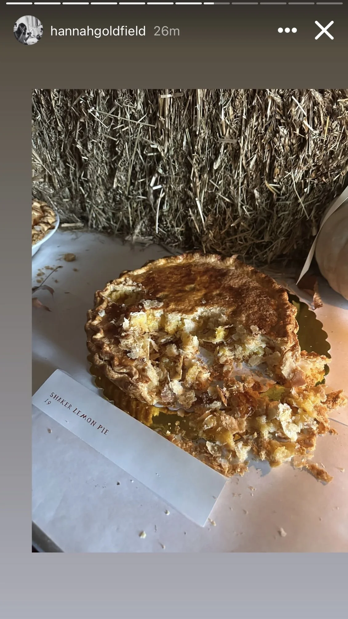 A partially eaten lemon pie on cloth-covered table with the label "Shaker Lemon Pie" placed on the table with a hay bale background.