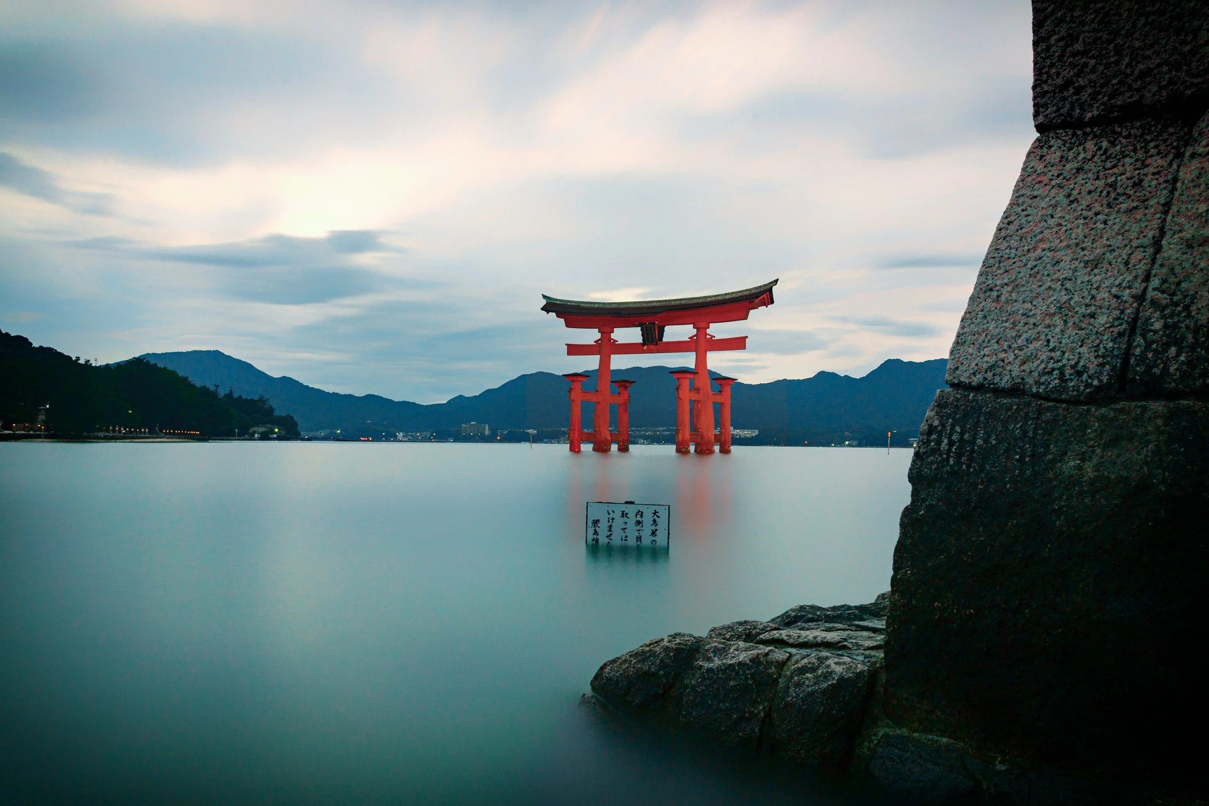 Torii japonés rojo en el agua frente a las montañas, símbolo de umbral espiritual y conexión con lo sagrado en la cultura japonesa