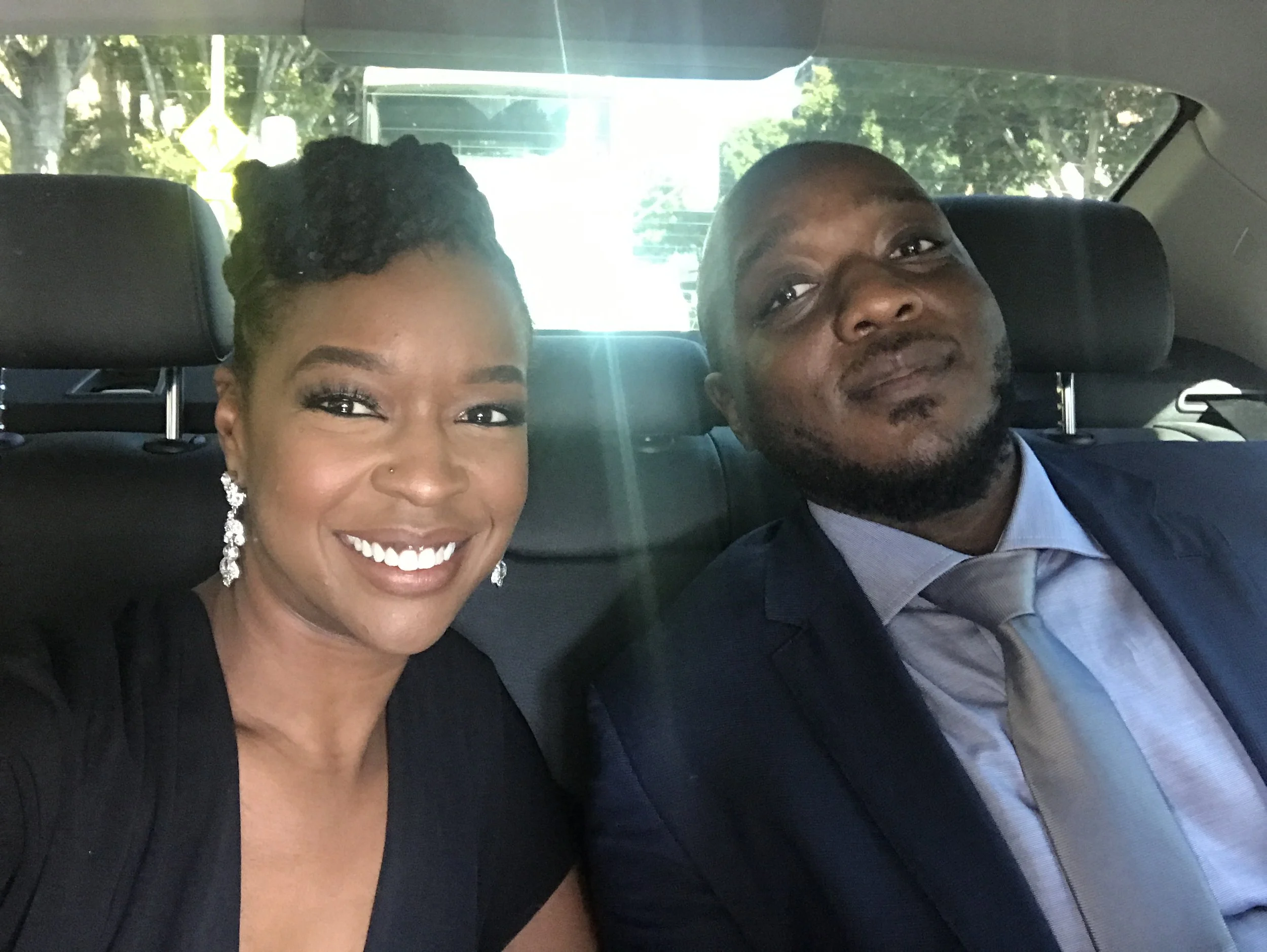  Rachel Cato and James Casey smiling in a photograph taken in the backseat of a car. Rachel is in a black dress, James is in a blue shirt, silver tie, and dark jacket for the 59th Grammy Awards. 