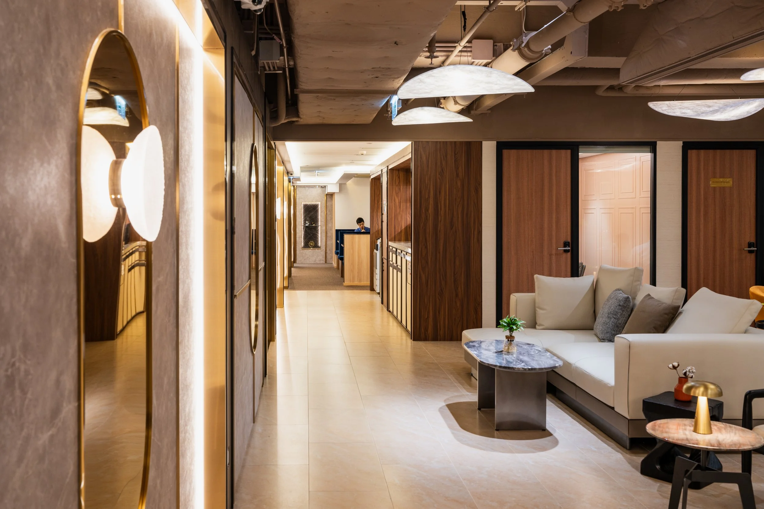 Modern hotel lobby with a white sofa, marble coffee tables, wooden walls, and decorative lighting.