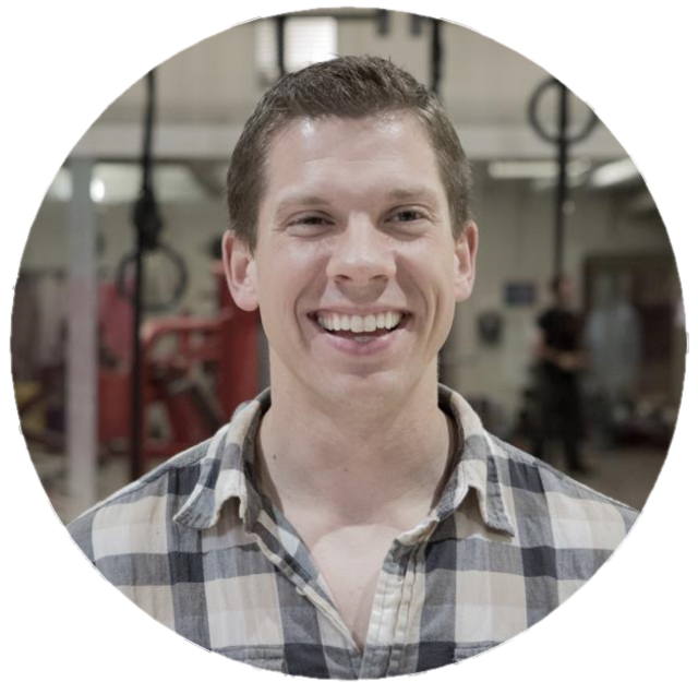 Smiling young man with short hair wearing a plaid shirt in a gym with workout equipment in the background.