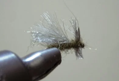 Close-up of a fishing fly with white and gray synthetic fibers held by a hand or tool.