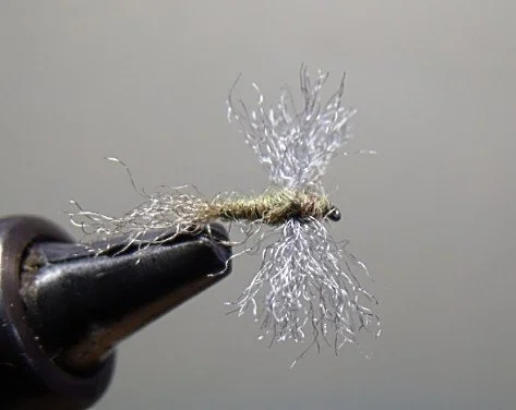 Close-up of a metallic fishing fly hook with an intricate, silver treble hook design.