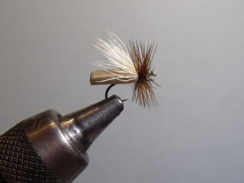 Close-up of a fishing fly tied to a metal hook, held in a black vise, used for fly fishing.