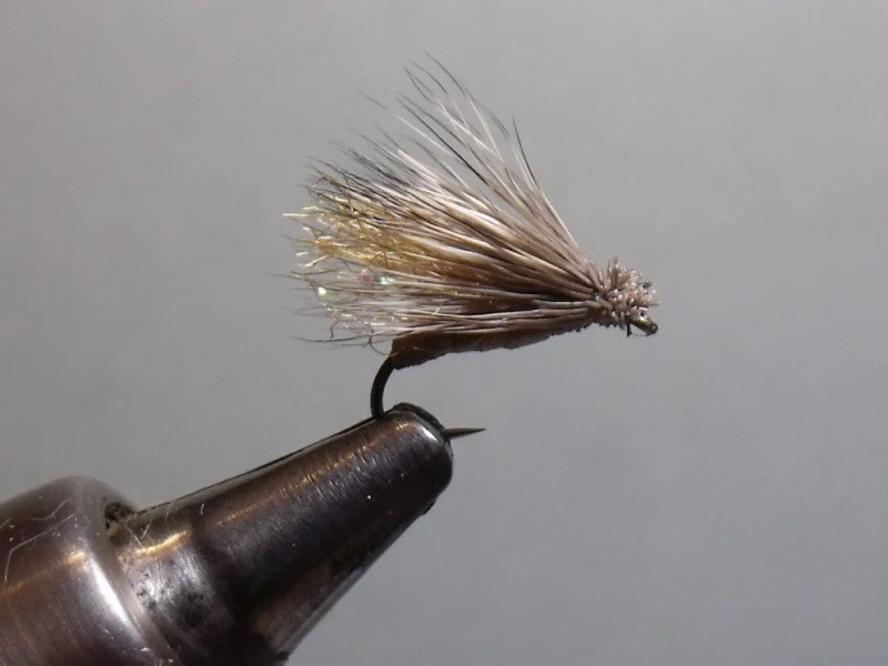 Close-up of a fishing fly on a metal vise tool against a gray background.
