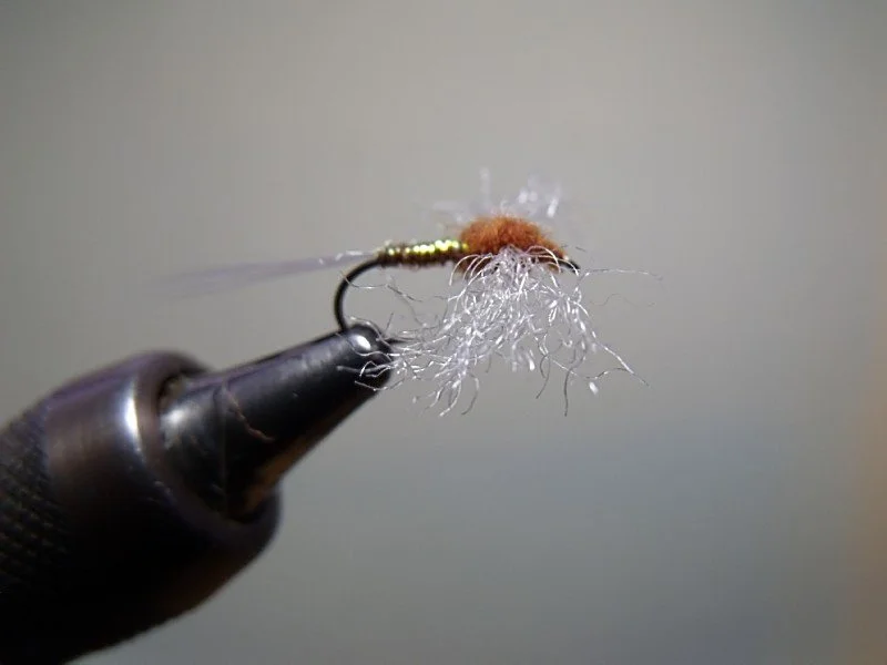 Close-up of a fly fishing lure with a foam body, attached to a hook, resting on a tool or vise.