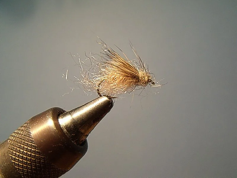 Close-up of a fishing fly held by a craft knife.