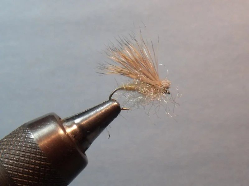 Close-up of a fishing fly with a hook, attached to a black-handled tool, used as bait for fishing.