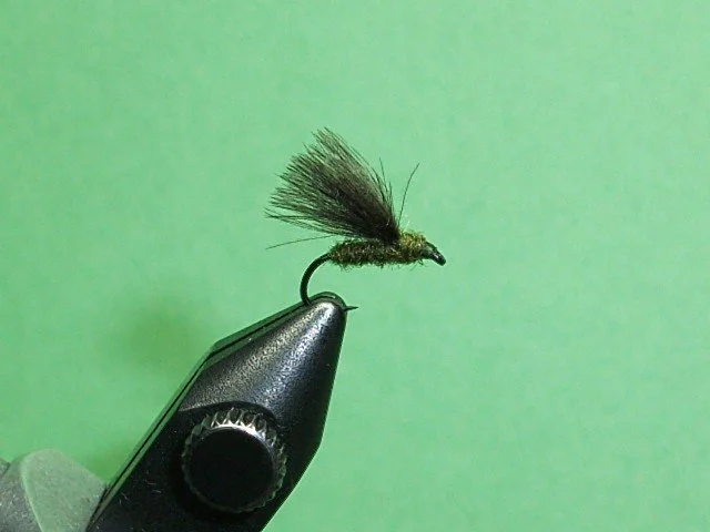 Close-up of a fishing fly tied to a hook, resting on a black object with a green background.