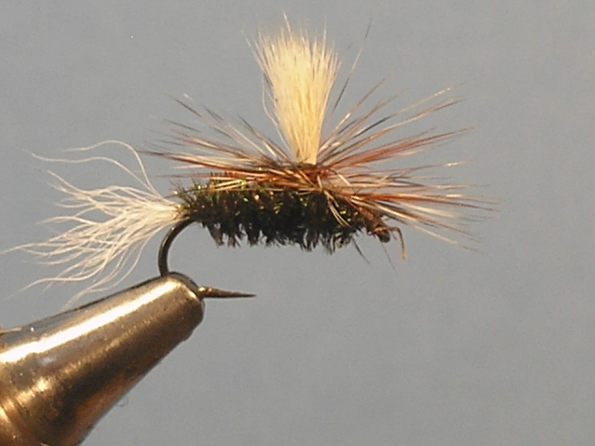 Close-up of a fly fishing lure held in a person's hand against a plain background.