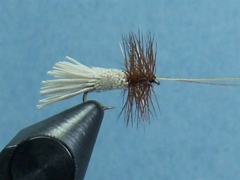 Close-up of a fishing fly on a black handle against a light blue background.