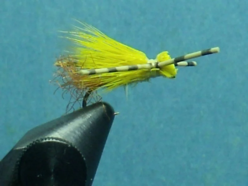 Close-up of a yellow and black fishing lure designed to resemble a small fish or bait, attached to a black fishing line against a blue background.
