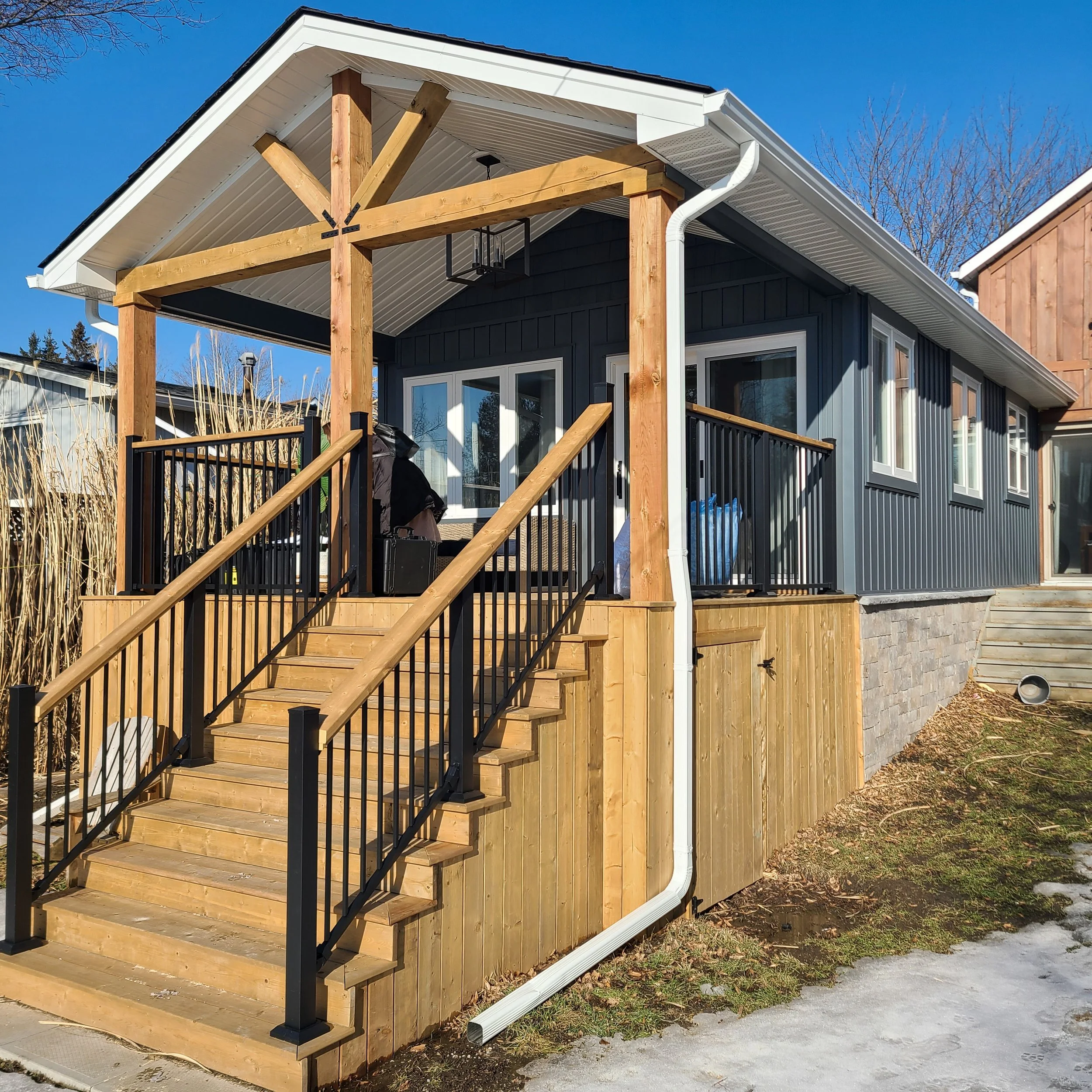 A completed home addition featuring a covered wood porch and dark siding, finished during the winter in Waterloo Region by Catalyst General Contracting.