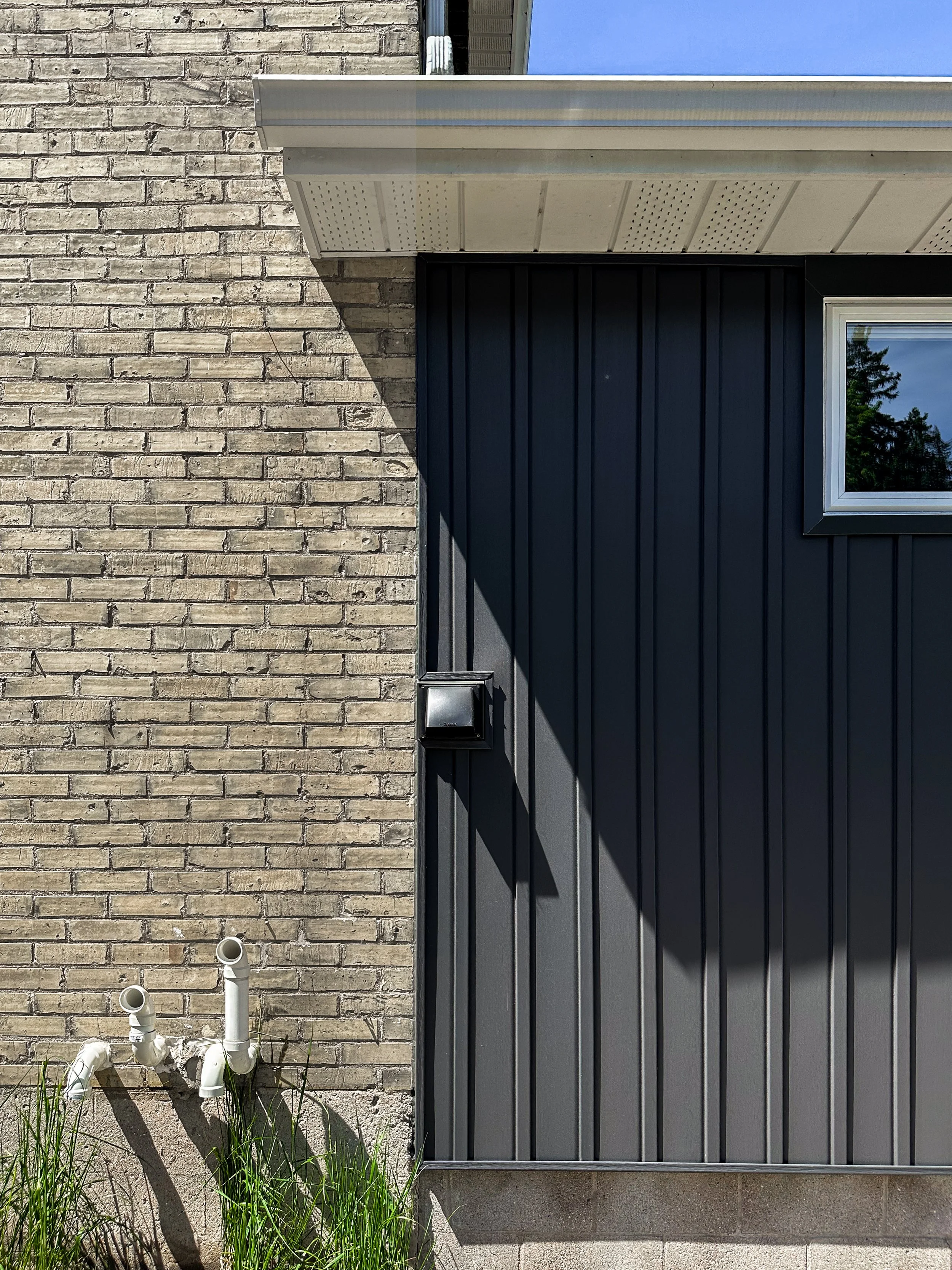 Exterior home update in New Hamburg highlighting the seamless transition between the home's historic yellow brick and new modern dark vertical siding.