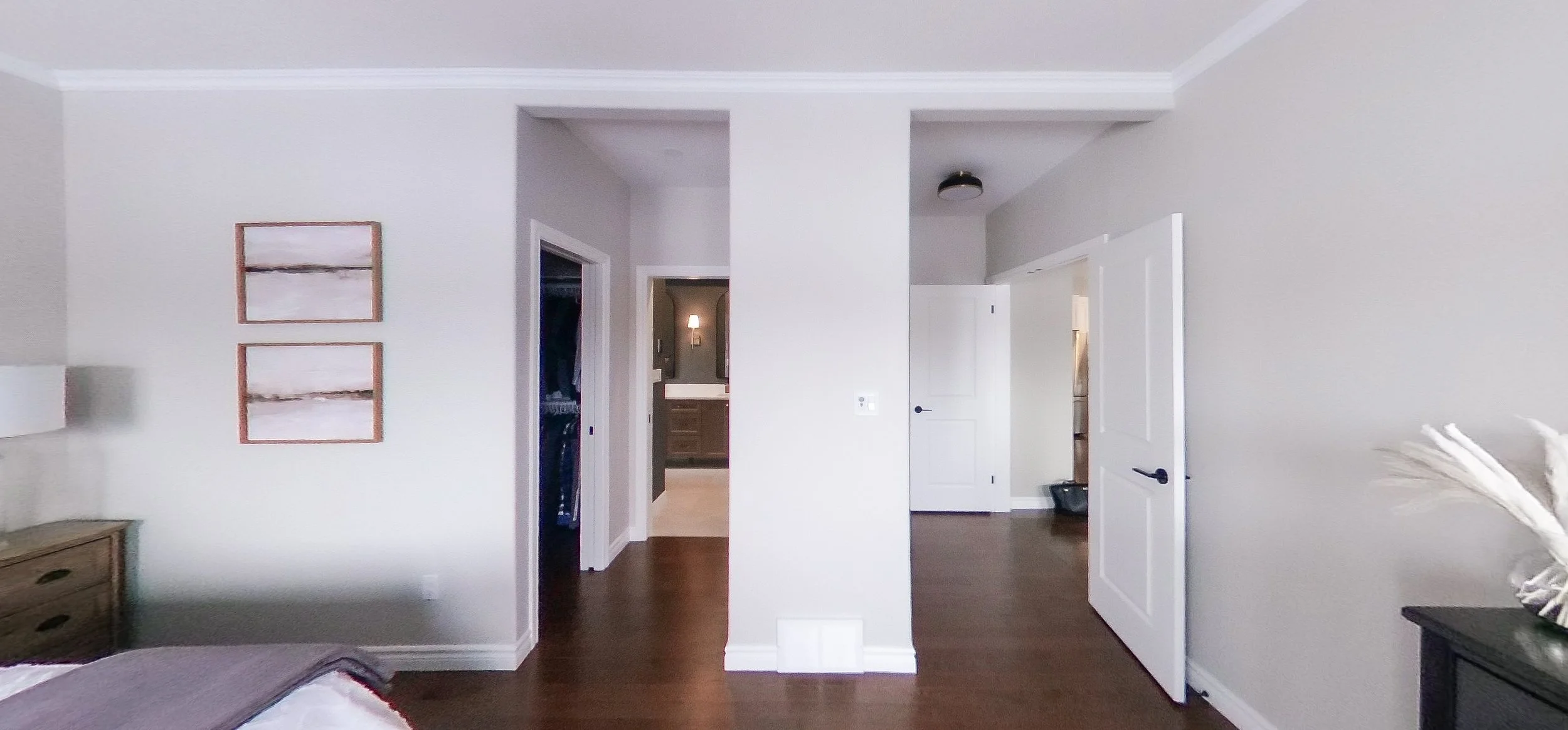 A wide view of the newly reconfigured primary suite showcases the bright, airy bedroom retreat. Continuous dark hardwood floors seamlessly connect the space, leading past the custom walk-in closet directly into the moody, organic modern ensuite bathr