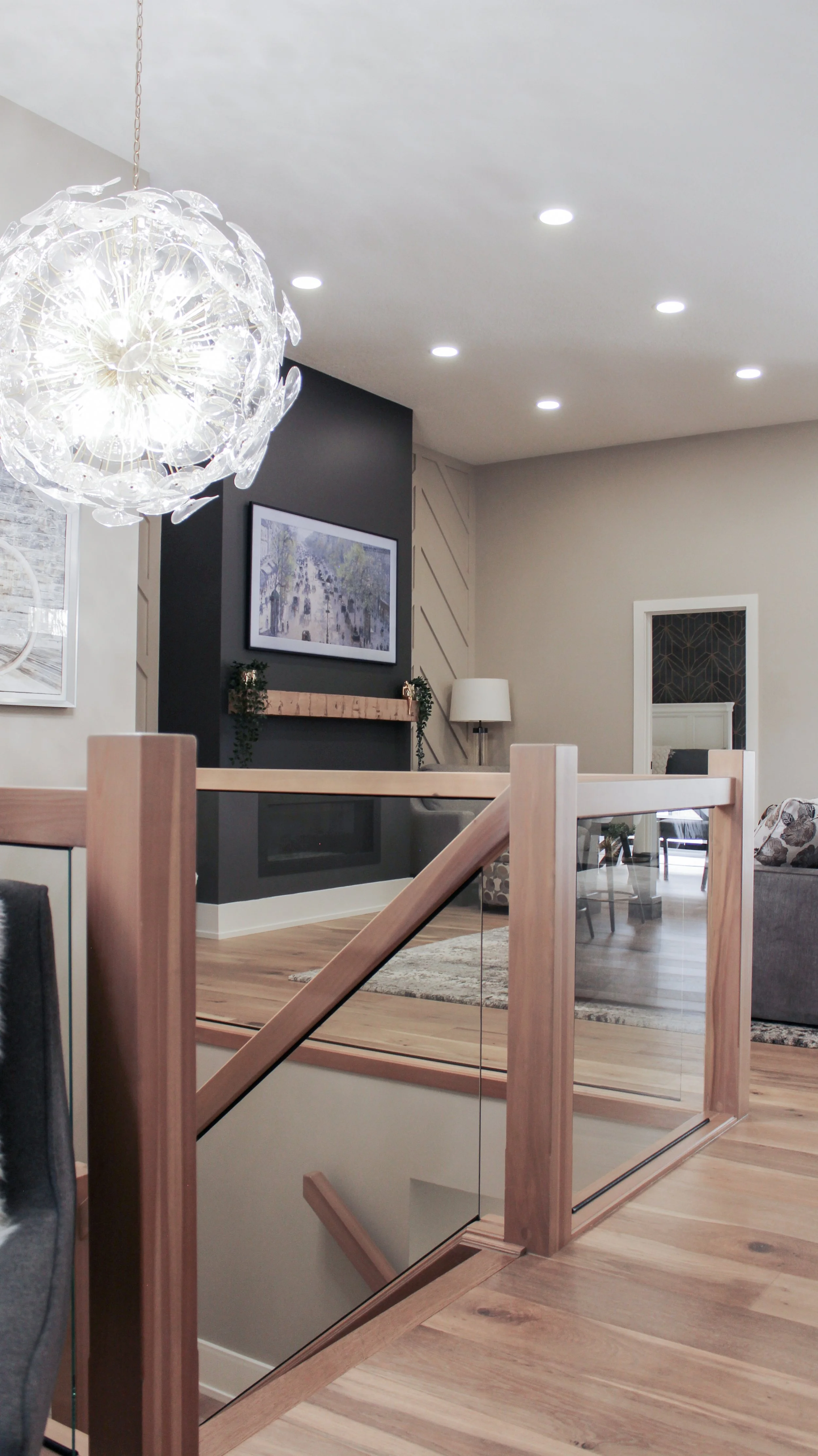 View from the top of a wood and glass staircase looking into a renovated living room with a feature fireplace.