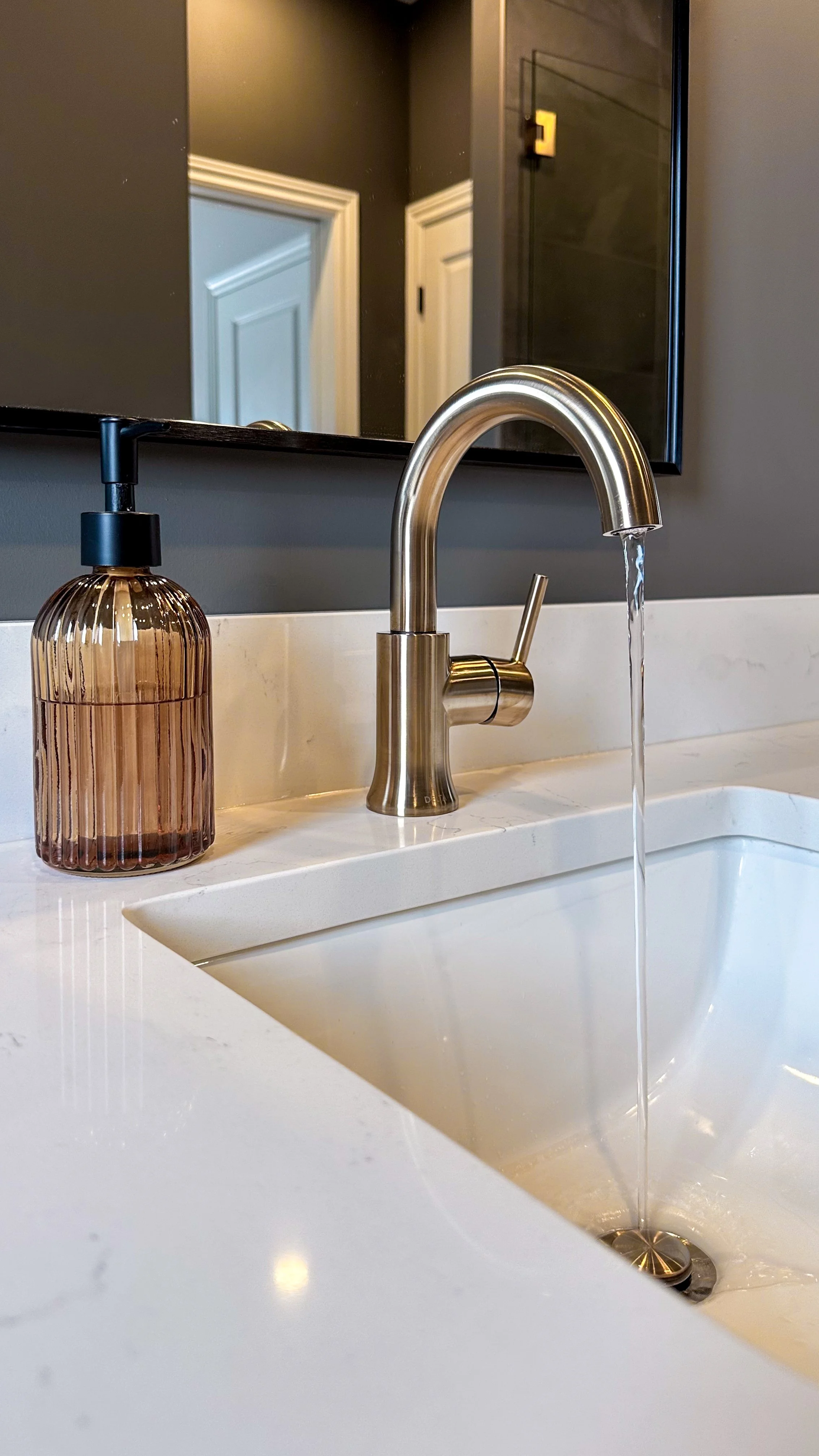 Clean, modern details make all the difference. A sleek brushed brass bathroom sink faucet and amber glass soap dispenser sit beautifully perfectly on the crisp white quartz countertop.