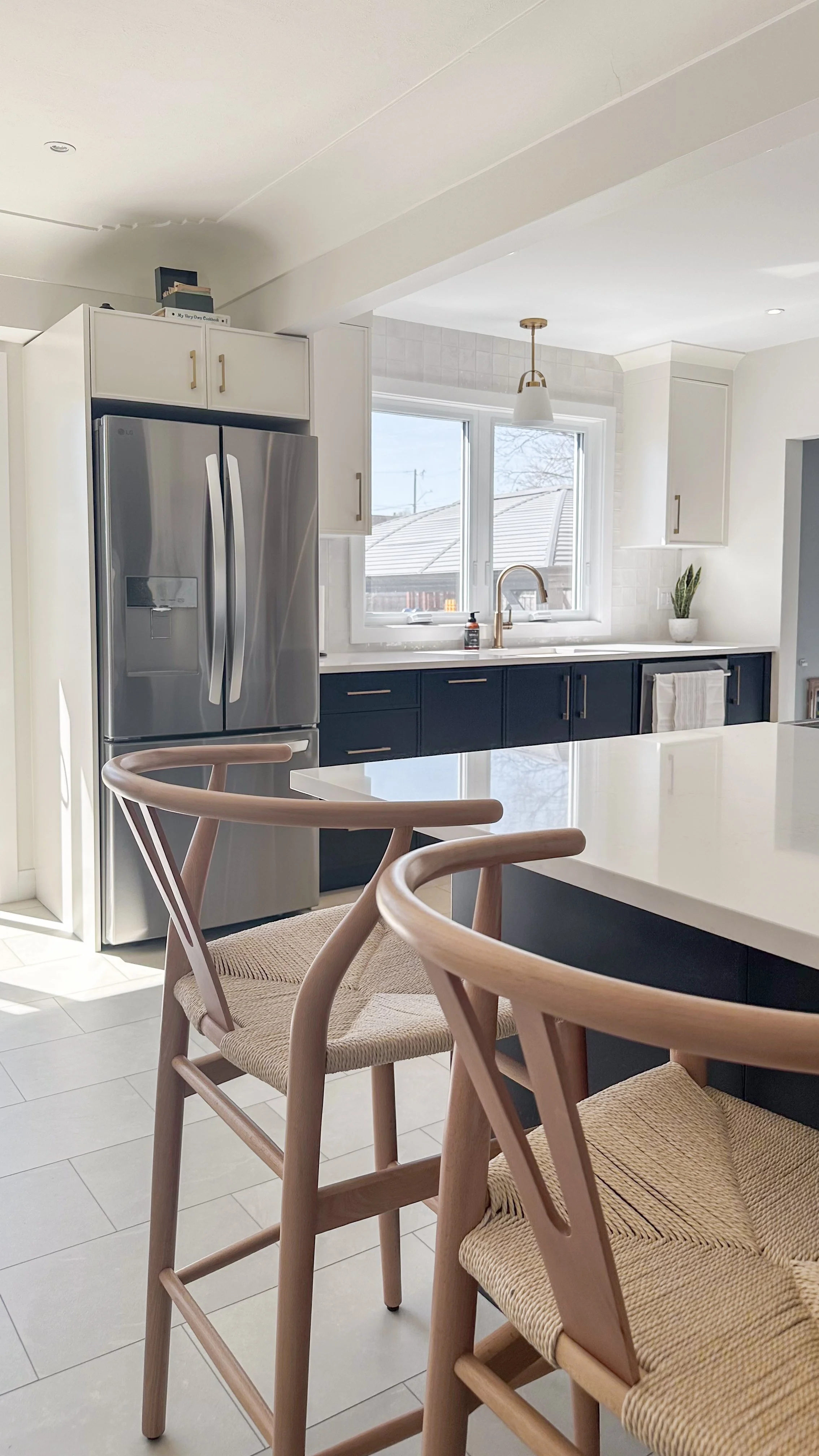 By relocating the bulky stainless steel fridge to the end of this run, we instantly opened up sight lines from the primary working zone. Deep charcoal lower cabinets ground the space, beautifully complementing the woven wood barstools at the island.