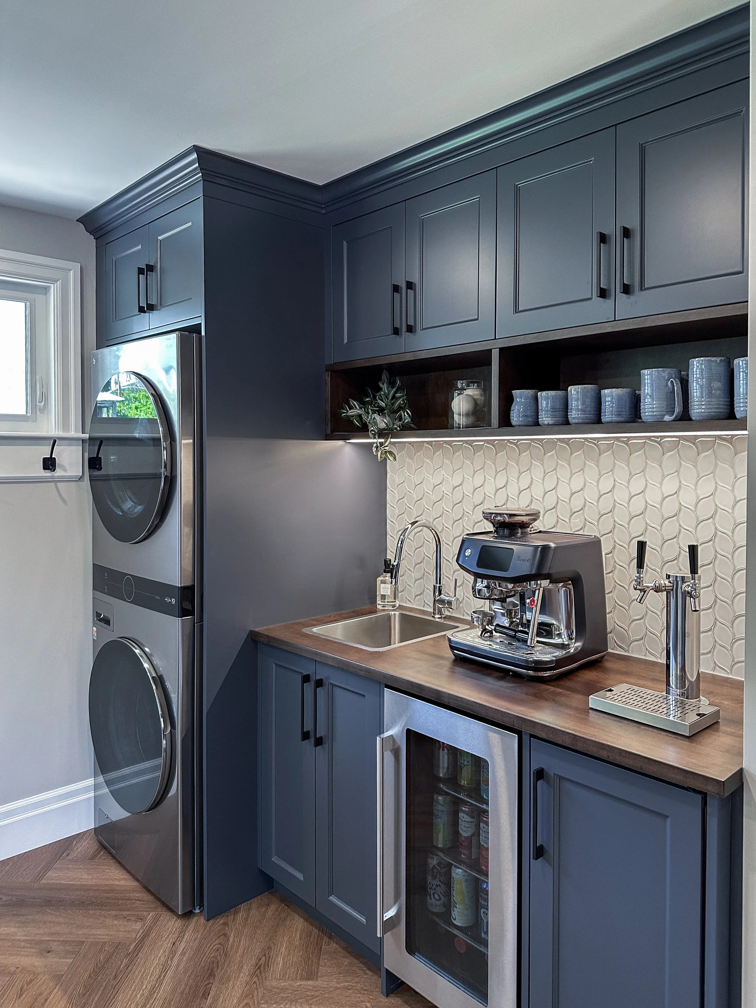 Custom laundry room renovation in New Hamburg featuring slate blue cabinetry, a built-in espresso station, and a beverage fridge.