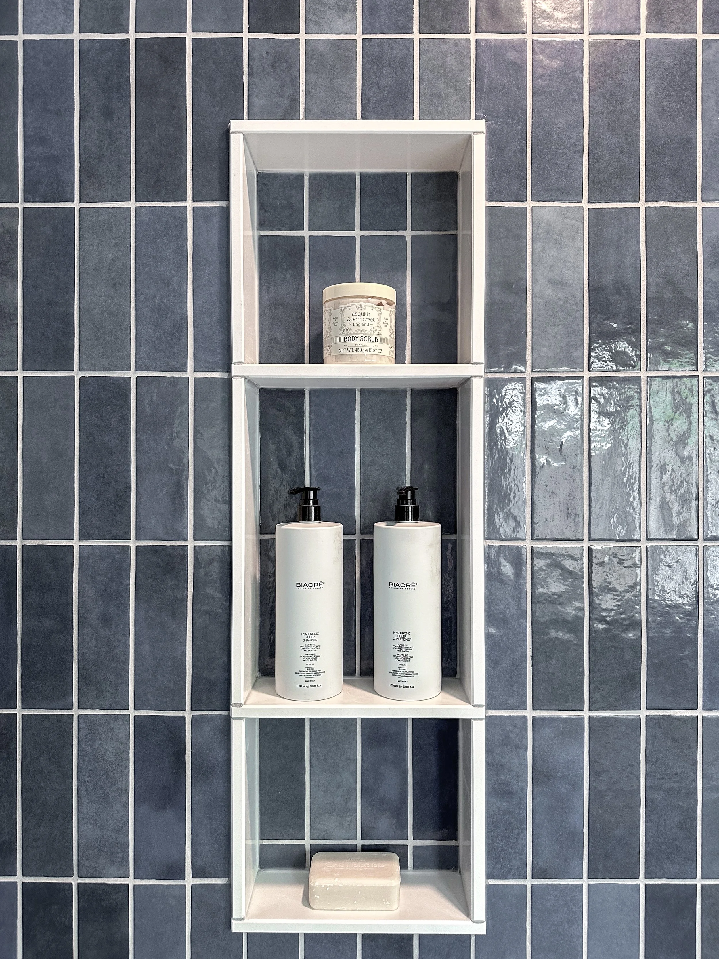 Custom shower niche in a Kitchener bathroom renovation highlighting striking vertical blue wall tile and built-in white shelving.