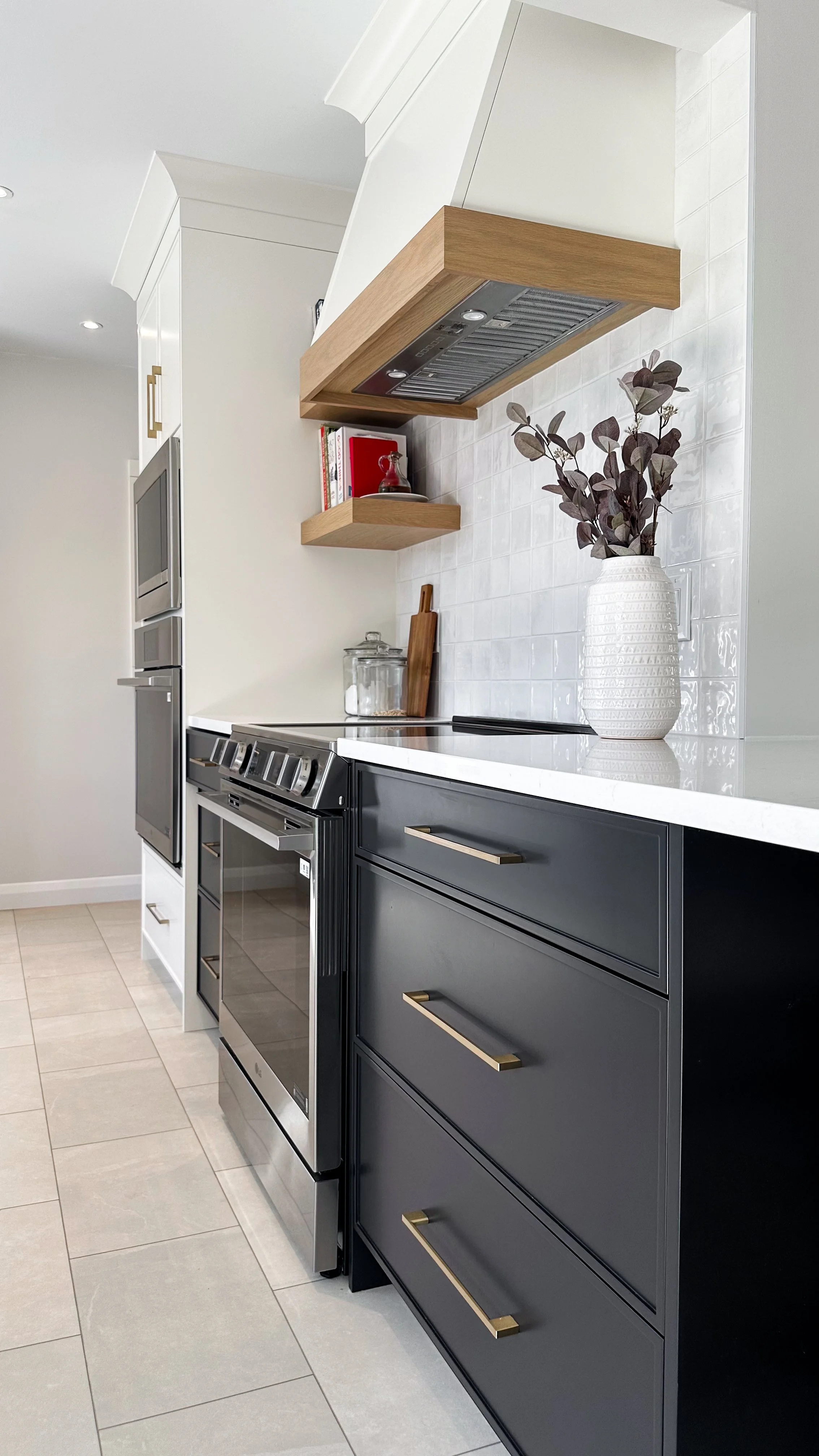 The new primary cooking zone features deep charcoal drawers for easy access to pots and pans, anchored by a custom wood-trimmed range hood. The glossy zellige-style backsplash and floating wood shelves bring in that perfect touch of organic modern wa