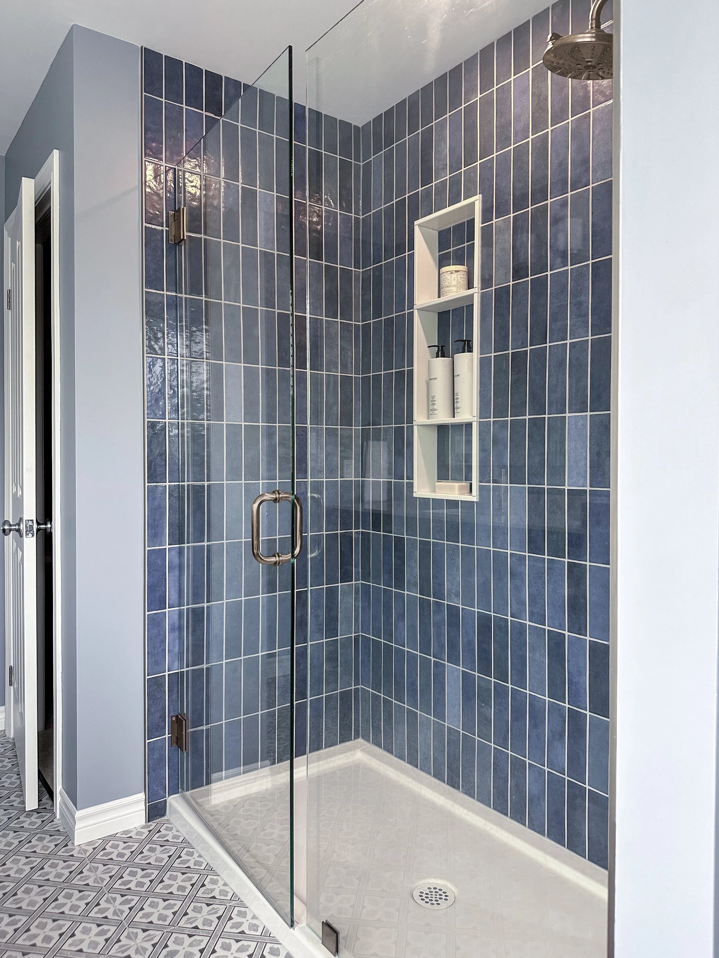 Custom walk-in shower renovation in Kitchener showcasing vertical blue tile, a glass enclosure, and patterned floor tile.
