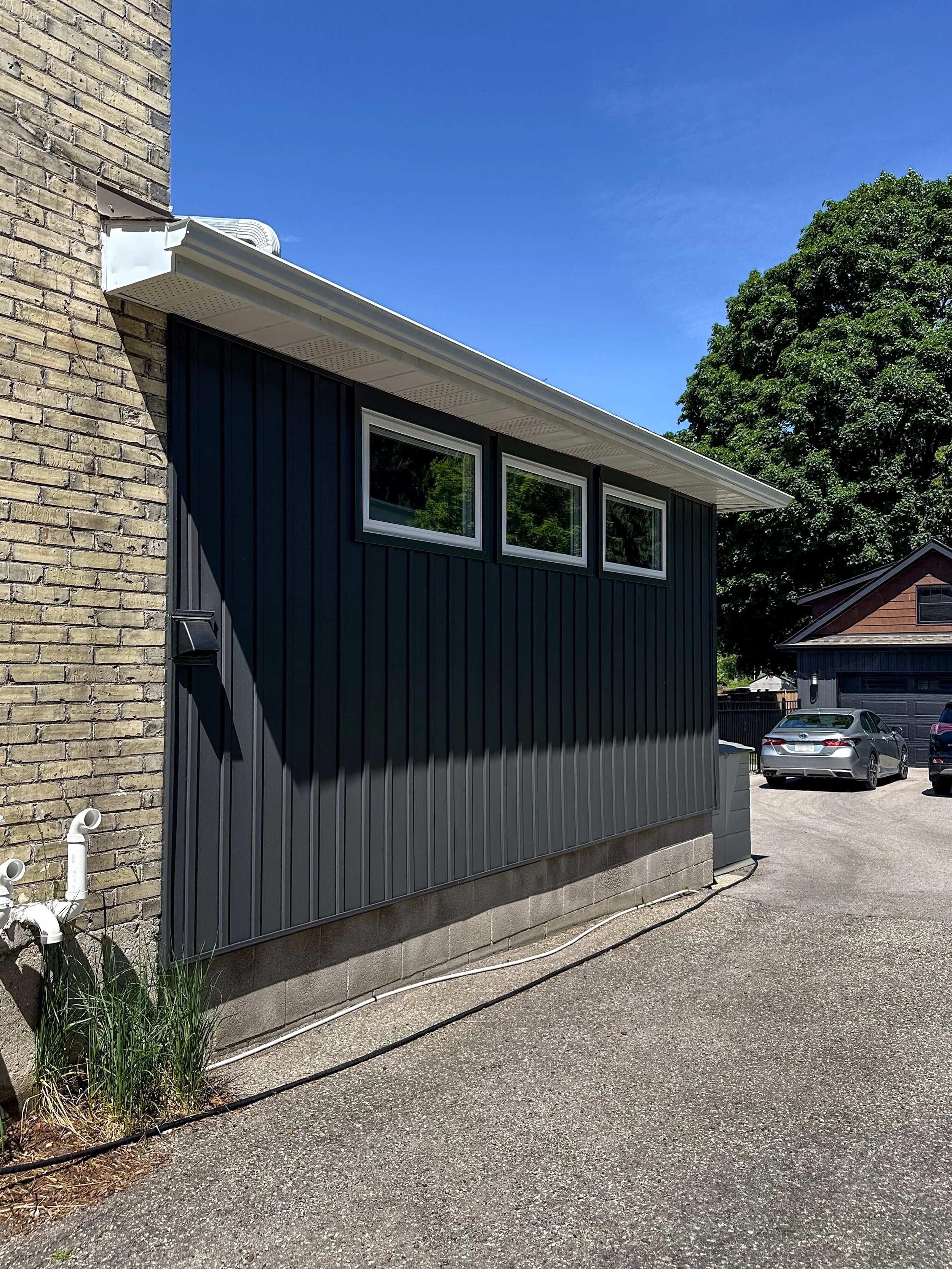 Exterior home renovation in New Hamburg featuring new dark vertical siding and custom windows to modernize an existing mudroom footprint.