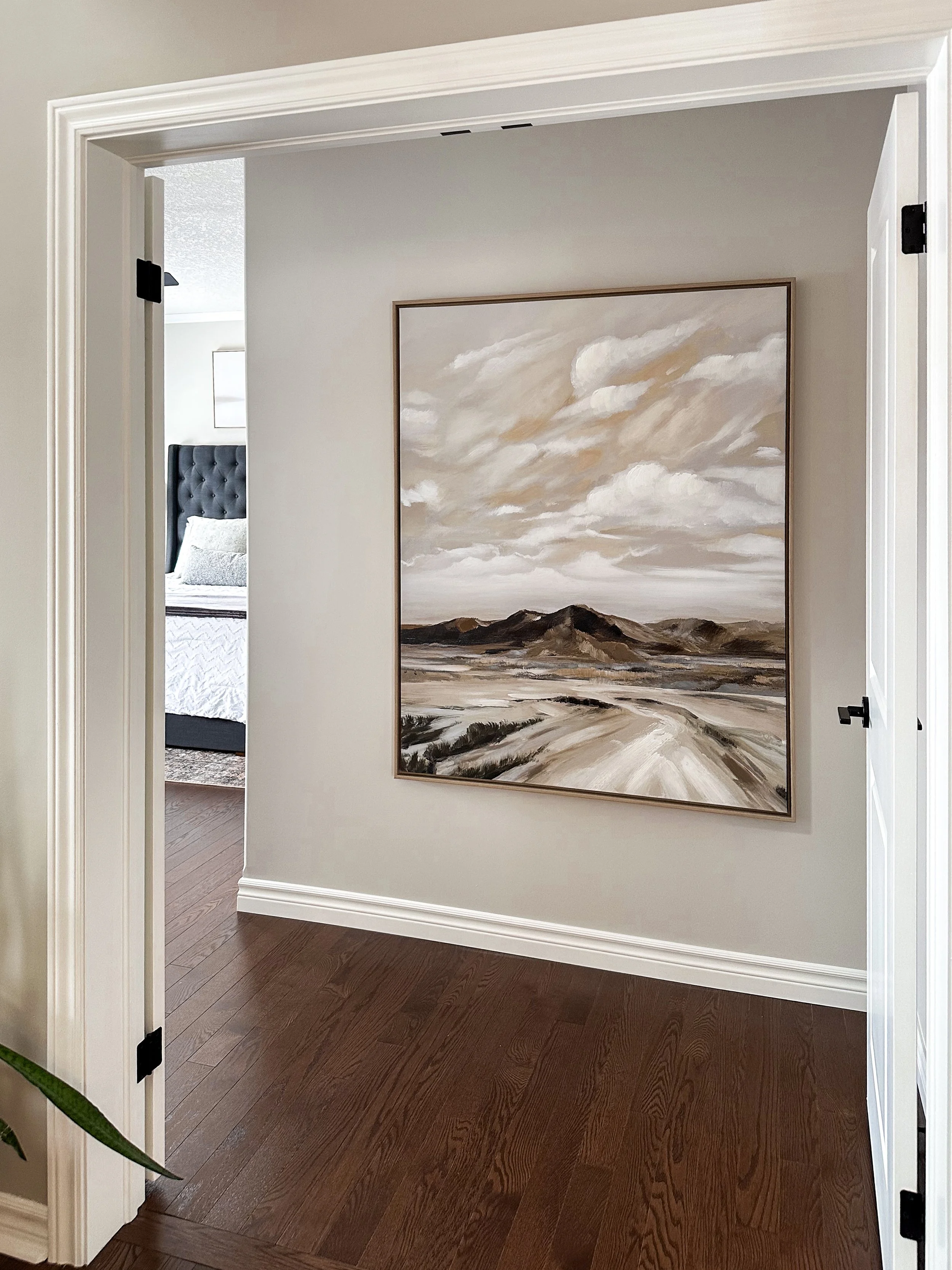 Primary suite entrance showcasing a large, organic modern landscape painting, complementing the dark hardwood floors and leading into a bright bedroom retreat.