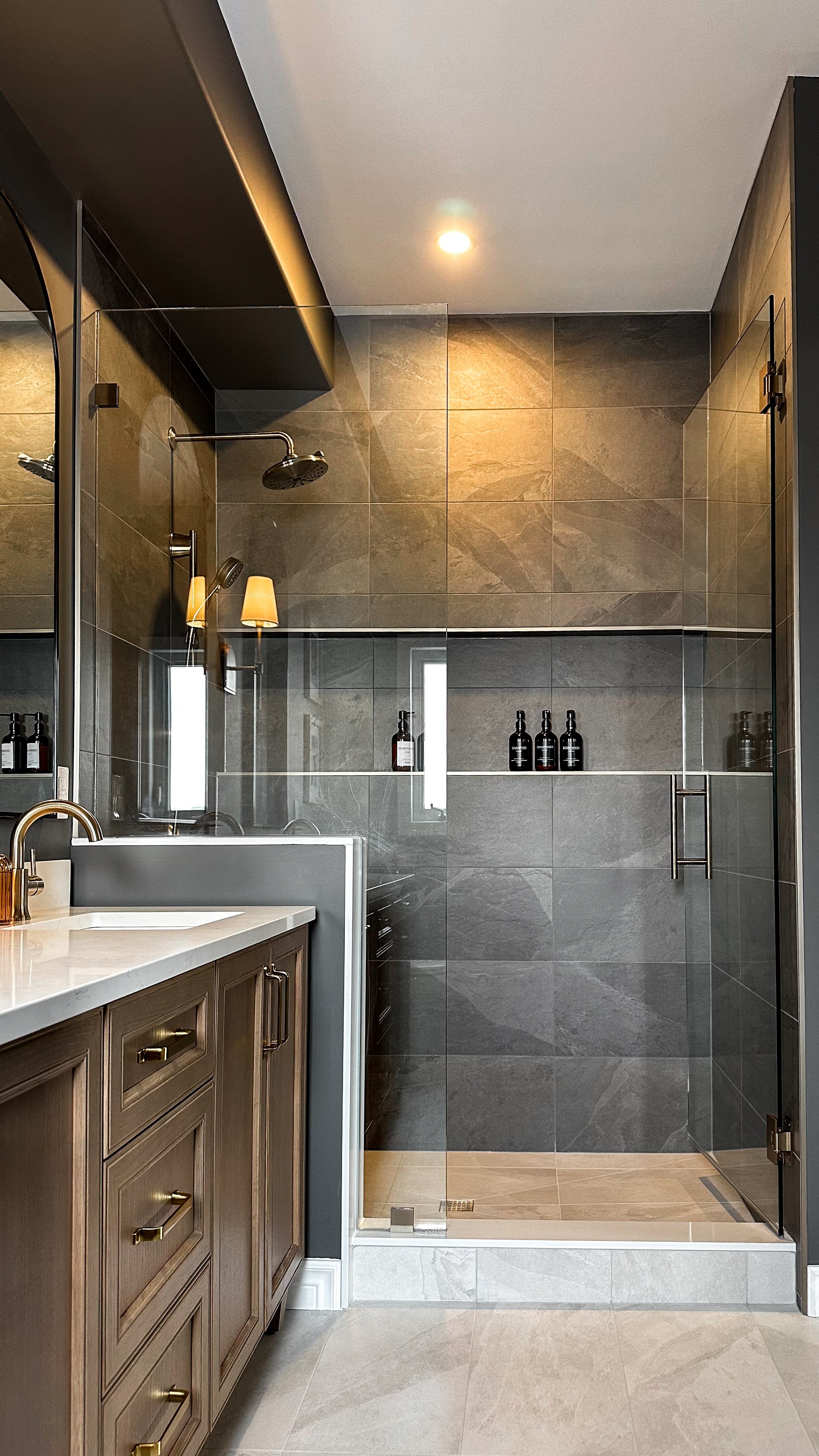 A custom walk-in shower features large-format, earthy stone-look tiles and an expansive horizontal built-in shower niche to keep bath essentials perfectly organized.